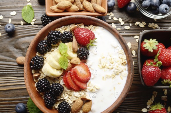 Flat lay top view at Fruit healthy muesli with banana strawberry almonds and blackberry with yogurt in clay dish on wooden kitchen table