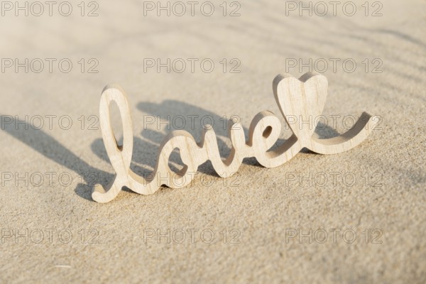 Wooden word love on sandy beach background. Concept of romantic holiday anniversary, proposal, valentines day greeting card, postcard. Letter text in tropical vacation Sand surface. Deep shadows Love is all you need