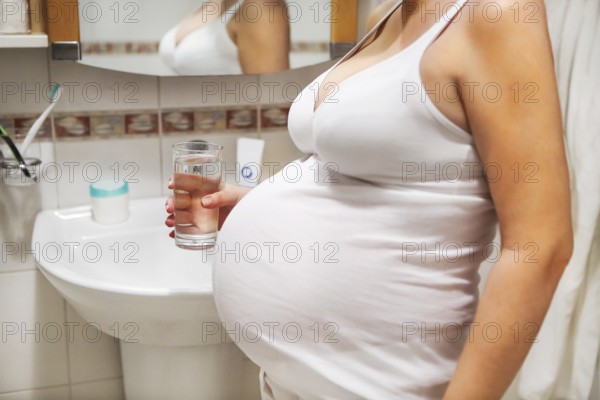 Pregnant woman with glass of water in the bathroom