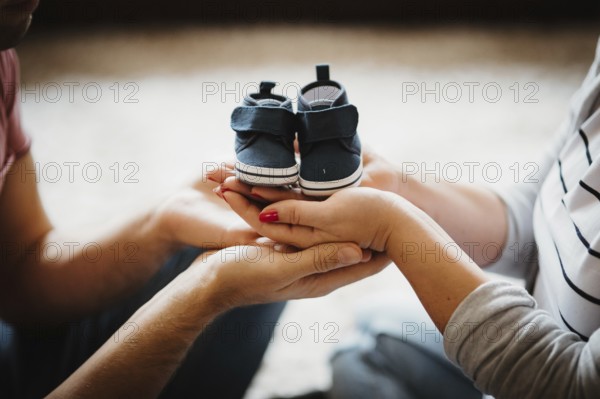 Young future parents holding baby booties shoes in their hands