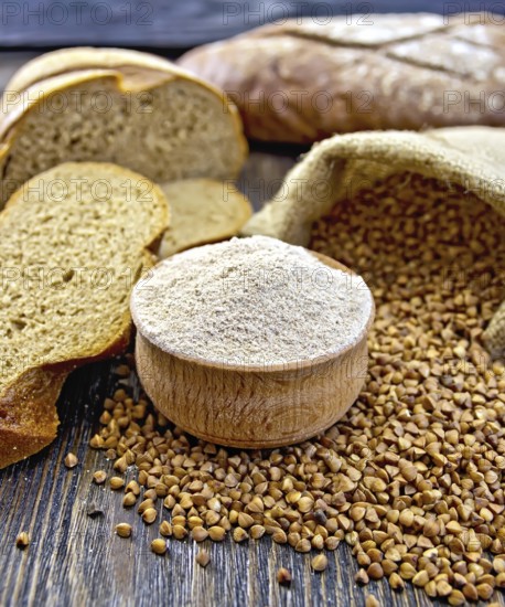 Buckwheat flour in a wooden bowl, buckwheat in the bag, the bread slices on a wooden boards background