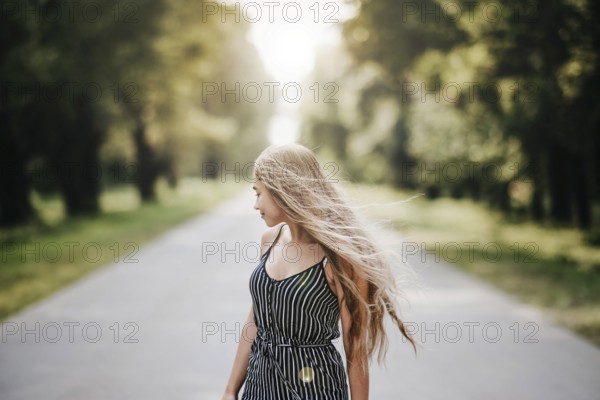 Woman facing sideways on a quiet road, her long hair flowing, creating a thoughtful and solitary summer mood