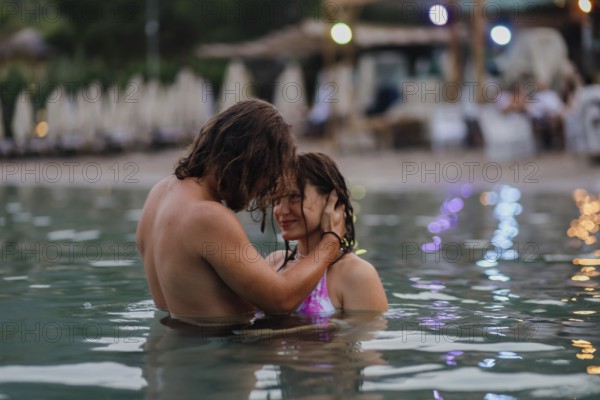 Couple affectionately interacting in water, surrounded by soft bokeh lights in the evening