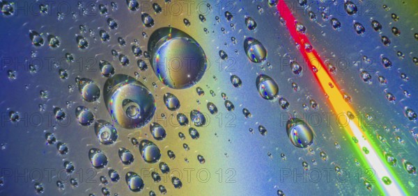 Beautiful closeup of water droplets floating on blueish silver background with rainbow colors dissecting the background