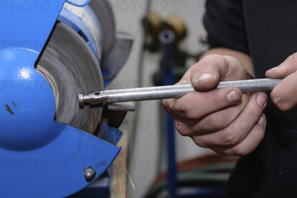 Skilled worker working on metal on a bench grinder - close-up