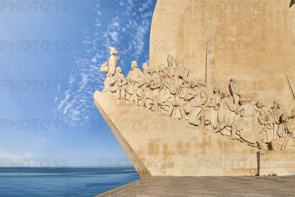 Lateral view of Monument of Discoveries, Padrao dos Descobrimentos, to Age of Discoverys haped as ship with statues of Prince Henry the Navigator and great people of Portuguese seafarers history, Lisbon, Portugal, at clear blue sky and sunrays on day, Europe