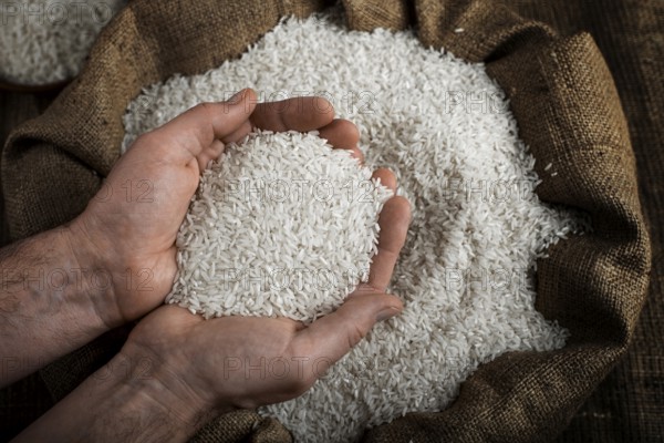 Human hands holding handful of rice over burlap sack