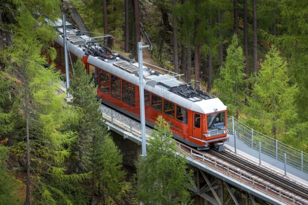 Zermatt, Switzerland, October 7, 2019: Gornergrat red tourist train on the bridge, village houses and Swiss Alps panorama, Europe