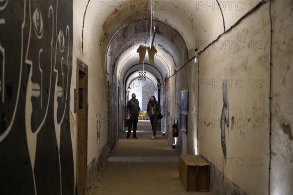 MAUSA VAUBAN, Museum of Urban Art and Street Art, Neuf-Brisach Fortress, France, Europe, Long underground corridor with gloomy wall art and two people in the background, Europe