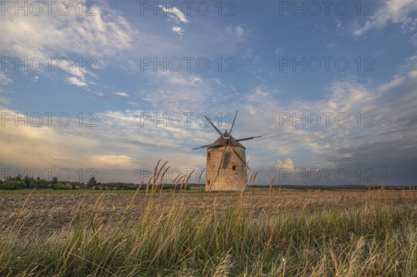 Windmill with wooden sails in a landscape with fields. Meadows and flowers appear in the sunset. Landscape shot in nature with a windmill. Historically atypical for the Balaton region in Hungary