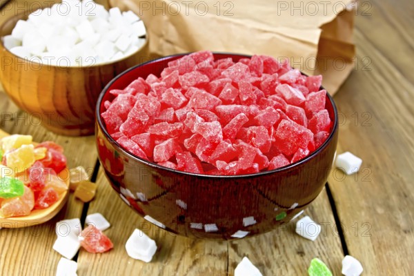 Candied papaya and coconut in bowls, colorful pieces of candied fruit in a spoon on a wooden boards background