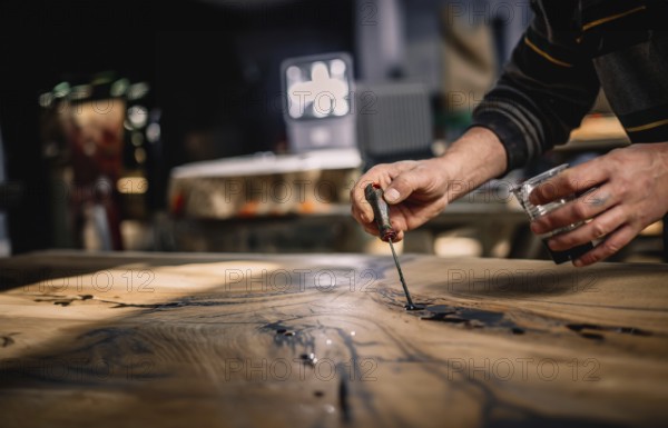 Close-up of hands expertly applying a tool to a wood surface under warm lighting in a shop setting