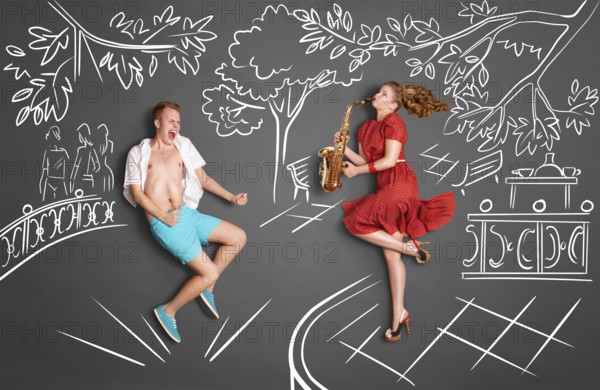 Love story concept of a romantic couple against chalk drawings background. Woman playing serenade on saxophone in a city park for her lover