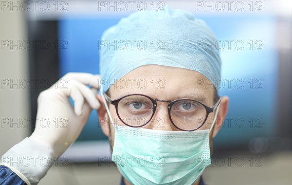A surgeon wearing glasses and a mask with a focused expression