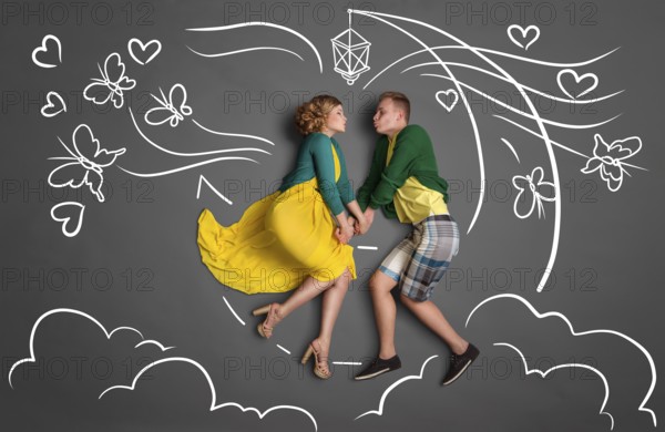 Happy valentines love story concept of a romantic couple sitting on the moon, holding hands and kissing against chalk drawings background of a night sky with butterflies