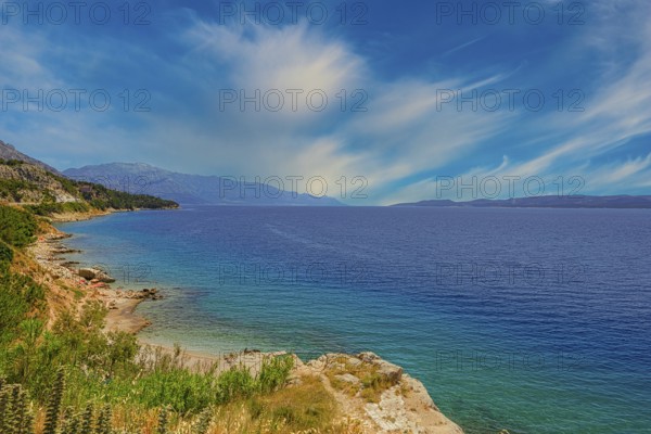 Coastal landscape with blue sea and green shore, peaceful sky with cloud patches, Makarska coast Dalmatia Croatia