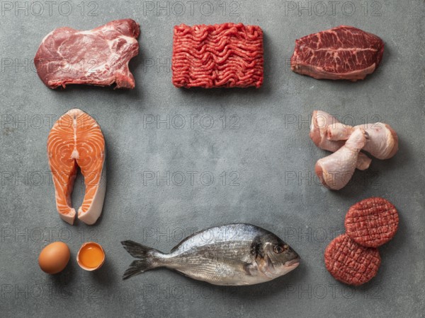 Carnivore or keto diet concept. Raw ingredients for zero carb or low carb diet - meat, poultry, fish, eggs and copy space in center on gray stone background. Top view or flat lay