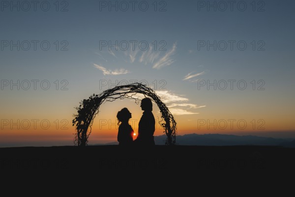 Silhouettes of bride and groom holding hands near the wedding arch at sunset at the wedding ceremony.