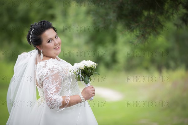 Fat bride with a wedding bouquet on a summer background