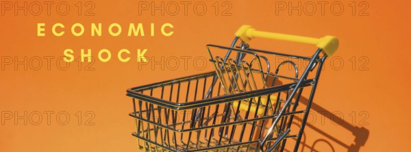 ECONOMIC SHOCK text Empty shopping trolley cart on colorful orange background. Online shopping, buy mall market shop consumer concept. Small toy supermarket grocery push cart. Rising food cost, grocery prices shortage mass hunger. Inflation