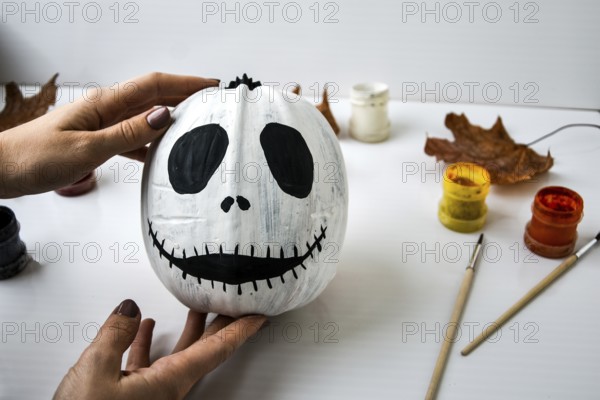 Woman paints face on orange pumpkin for Halloween. Autumn leaves. Diy children craft. Do it yourself. Autumn party decorations