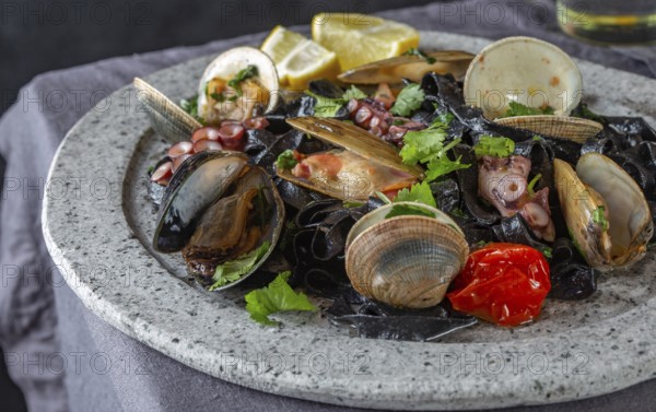 Food, Seafood black fettuccine fehttuchini. Black pasta with squids, octopus clams, mussels on stone plate. Gourmet dish