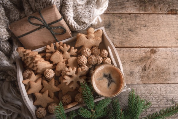 Cozy Christmas with a tray full of gingerbread, cookies and a cup of coffee, a fir twig, a gift, and a wool scarf, on a rustic table