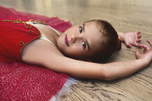 Side view portrait of a cute Beautiful little ballerina in a performance dress lying on the floor of the dance hall
