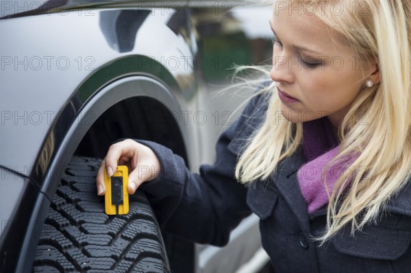 A young woman measures the tread depth of her car tyre. The right depth in the tread of a tyre can prevent accidents