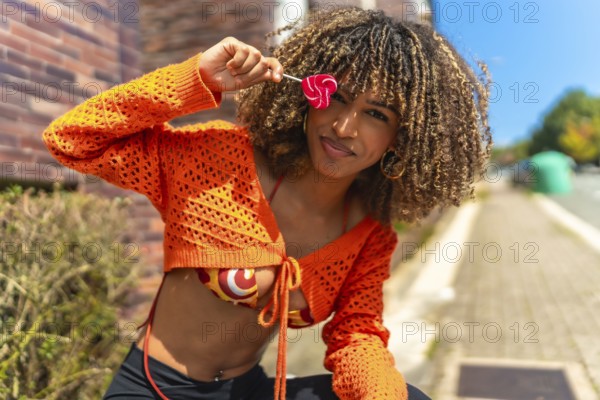 Latin beauty woman flirting and playing with heart shaped lollipop sitting outside a house in the street