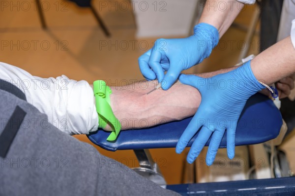 Close-up of the hands of a doctor carefully inserting a needle into the arm of a blood donor