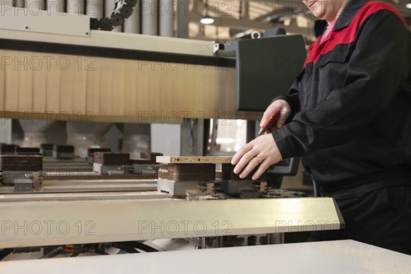 Side view of crop unrecognizable worker processing piece of plywood during manufacturing process at furniture factory