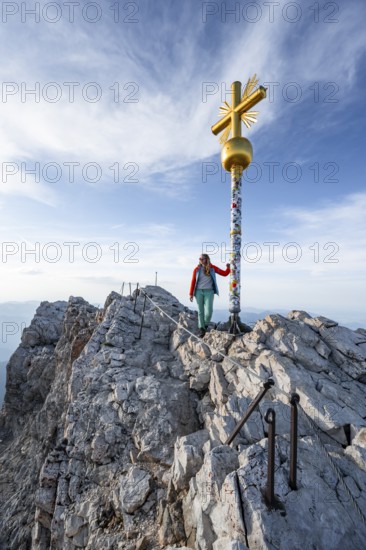 Mountaineer in front of golden summit cross, summit of the Zugspitze, Wetterstein range, Bavaria, Germany, Europe