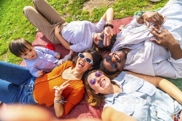 Group of cheerful multi ethnic friends enjoying a sunny day at the park taking a selfie while lying on a blanket