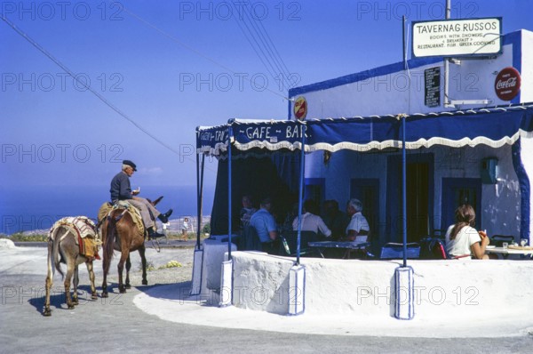 Man riding donkey past tourists eating lunch, Taverna Russos, Fira, Santorini, Santorini, Cyclades islands, Greece, Europe, 1972, Europe