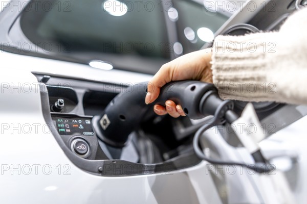 Close up of a hand plugging a charging cable into an electric vehicle at a car dealership, showcasing the transition to sustainable transportation