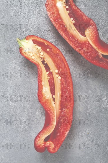 Fresh red peppers are sliced to reveal their bright interior, showcasing seeds and texture. The vibrant colors contrast against a smooth gray background, highlighting their freshness.