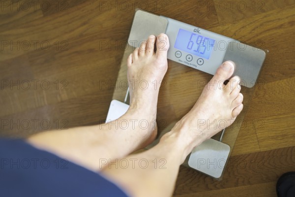 Symbolic photo on the subject of body weight. The feet of a 60-year-old person can be seen next to the weight display of a scale. Berlin, 13.08.2024