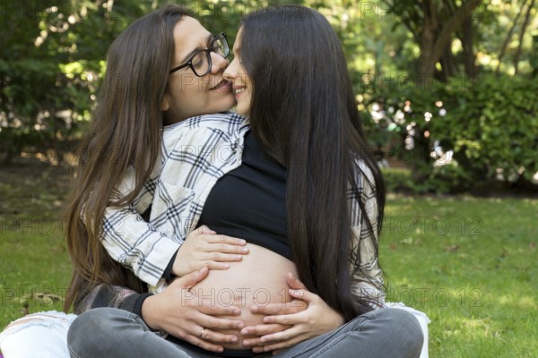 Portrait of affectionate pregnant lesbian couple relaxed at the park. Two happy girlfriends. Homosexual relationship. LGBT Community Pride. High quality photo