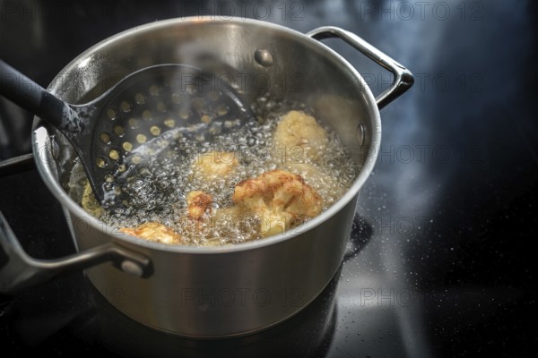 Deep frying cauliflower florets in a pot with boiling cooking oil on the stove, preparation of a tasty vegetable meal, copy space, selected focus, narrow depth of field