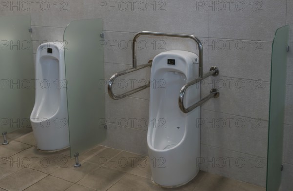 Porcelain urinal with handrails for use by disabled person next to non-disabled urinal in public restroom in South Korea