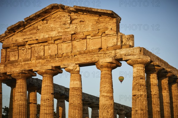 Sunset behind ancient columns of a temple with a clear sky, summer evening mood in Paestum, ancient town, 35 km south of Salerno.Founded by the Greeks around 600 BC, the city was given the name Paestum by the Romans in 274-273 BC.Important monuments from Greek and Roman times. The three large Doric temples are of particular importance. Europe, Italy. Campania. Salerno. Paestum