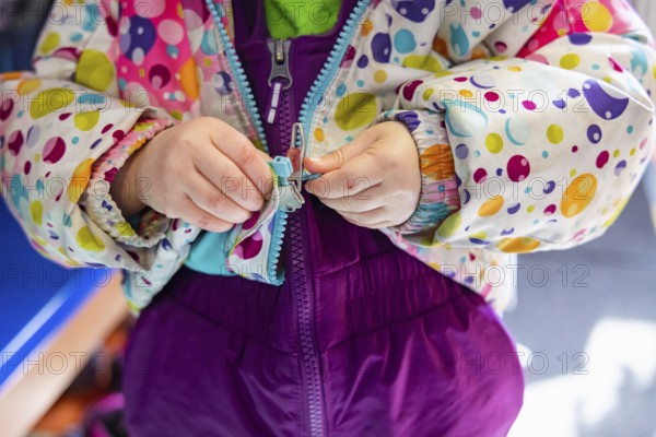 Close up shot on the hands of a kindergarten child struggling to latch and close the zipper of his winter coat before going outside in the wintertime
