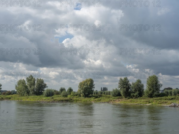 Calm river with grassy banks and trees in the background under a cloudy sky, zutphen, gelderland, netherlands