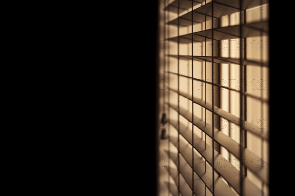 Horizontal shot of venetian blinds creating a moody and noir inspired atmosphere with light illuminating a dark room. Selective focus