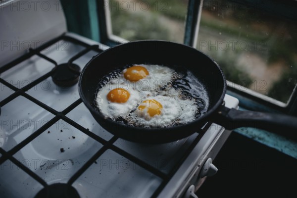 Frying pan with three eggs cooking on a gas stove beside a window