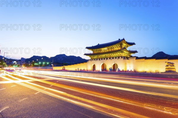 Colorful streaking headlights of cars passing in front of lighted gate of Gwanghuamun, entrance to historic Gyeongbokgung Palace at twilight in downtown Seoul, South Korea. Horizontal