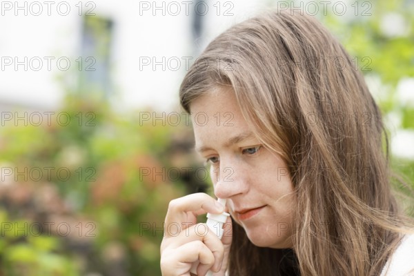 Young woman suffers from hay fever and sprays her nose outdoors, Freiburg, Baden-Württemberg, Germany, Europe