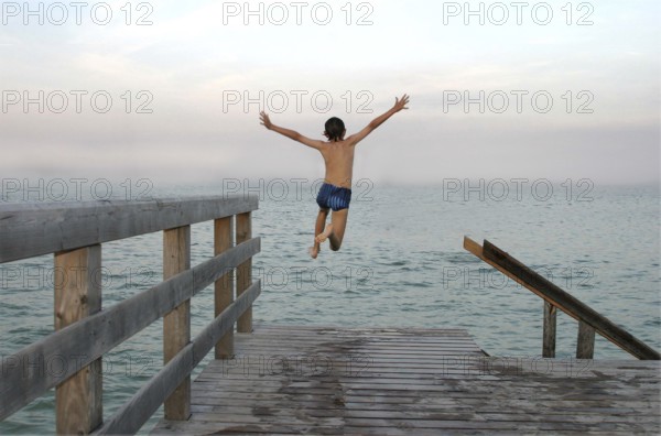 Boy jumps into water, wooden jetty