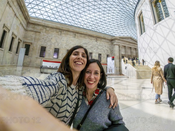 Two joyful female tourists capturing a selfie while enjoying their time in the stunning great court of the british museum in london